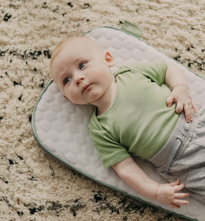baby in green onesie lying on white and blue polka dot bed